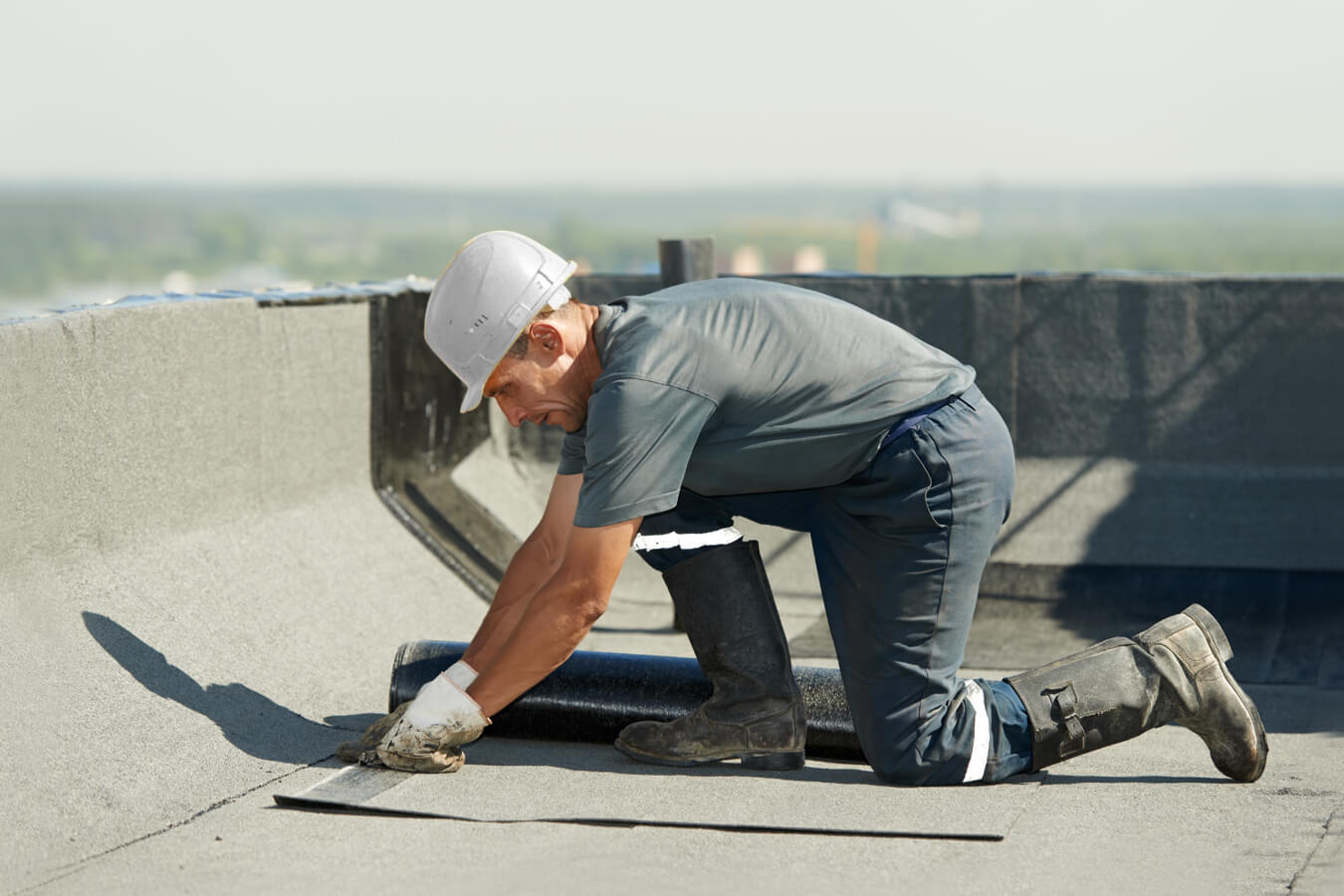 Worker positioning roofing material near the edge of a flat roof