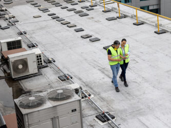 Two workers on a commercial roof beside rooftop equipment