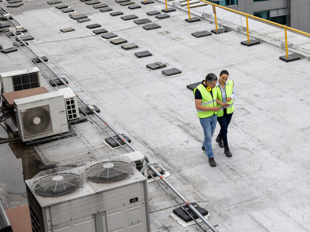 Two workers on a commercial roof beside rooftop equipment